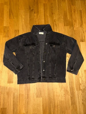 Svart jeansjacka från ASOS DESIGN - Snygg svart jeansjacka från ASOS DESIGN i klassisk modell med knappar framtill och två bröstfickor med lock. Jackan har en rak passform och är tillverkad i robust denim med coola sömdetaljer. 