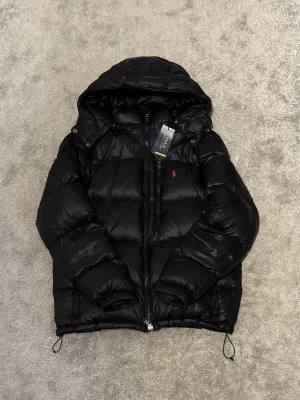 Polo Ralph Lauren - The Gorham Glossed Down Jacket - Säljer en glansig pufferjacka från Ralph Lauren som bara är använd en gång! Skick 10/10. Storlek M. Nypris: 6095kr. Kvitto finns!