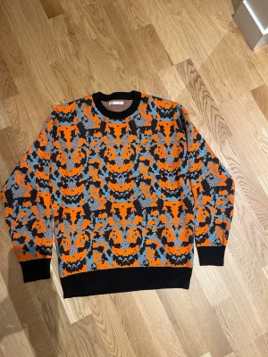 Orange och grå mönstrad tröja Zara stl M män  - Cool långärmad tröja från Zara i storlek M med ett unikt camouflage-liknande mönster i orange, grått, svart och blått. Tröjan har svarta ribbade muddar vid hals, ärmslut och nederkant. Perfekt för dig som gillar att sticka ut med färg och mönster. Aldrig använd 