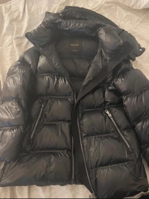 Svart pufferjacka från Massimo Dutti - Säljer en svart pufferjacka från Massimo Dutti med glansig finish och stor huva. Jackan har två snedställda fickor med dragkedja och kraftig frontzip. Perfekt för kalla dagar och har en riktigt schysst oversized look.