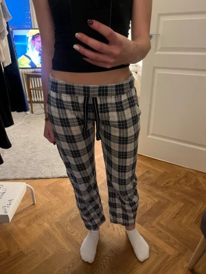Rutiga mjukisbyxor med snörning - Säljer ett par rutiga mjukisbyxor i svart, grått och vitt. Byxorna har elastisk midja med svart snörning och raka ben. Perfekta för chill dagar hemma. Mjukt och skönt material, klassiskt rutmönster och avslappnad passform. Har ett litet hål men som inte syns eller märks av, annars bra skick 🥰