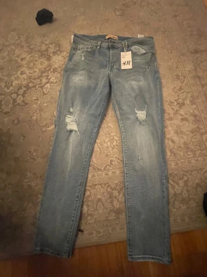 Ljusblå ripped jeans från H&M - Snygga ljusblå jeans från H&M med slitna detaljer och hål på båda benen. Modellen är smal och har klassisk femficksdesign. Perfekt för dig som gillar en avslappnad och trendig streetstil. Helt oanvänd och lappen är kvar🙌🏽💘