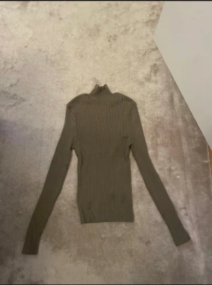 Ribbad beige polotröja från Zara - Säljer en ribbad beige polotröja från Zara i storlek M. Tröjan är figurnära med lång ärm och hög krage, perfekt att styla med jeans eller kjol. Materialet är mjukt och stretchigt, vilket gör den riktigt skön att bära.