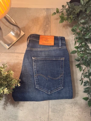 Mörkblåa jeans från Jack & Jones - Säljer ett par klassiska blå jeans från Jack & Jones med snygg tvätt och kontrastsömmar. Modellen har normal passform. Skinnpatch med logga bak i midjan. Perfekta för dig som gillar stilrena och bekväma jeans.