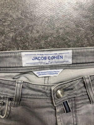 Grå jeans från Jacob Cohën - Snygga grå jeans från Jacob Cohën med klassisk femficksdesign och svart patch baktill. Jeansen har raka ben och är tillverkade i mjukt bomullstyg med en exklusiv känsla. Perfekta för dig som gillar stilrena och moderna jeans med italiensk touch. (Storlek 30 W) Rekkomenderas om du är runt 175 cm lång)