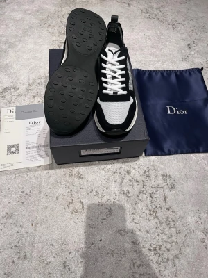 Dior B25 - Säljer ett par snygga Dior sneakers i svart och vitt med klassisk Dior-logga på sidan. Skorna har meshpaneler, mockadetaljer och vita snören. Sulan är platt och har rund tå. Kommer med originalkartong och dustbag. Perfekt för dig som gillar exklusiva märken.
