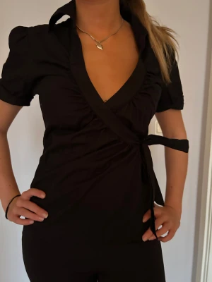 Svart omlottblus med kort ärm - Svart omlottblus med kort puffärm och krage. Snygg v-ringning och knyt i sidan för en bra passform. 💓💓