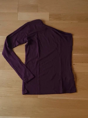 Vinröd topp - Vinröd one shoulder topp med lång ärm. Toppen har en tight passform och är tillverkad i ett mjukt, ribbat material som sitter skönt mot kroppen. 