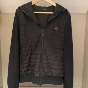 J.lindeberg cardigan - Svart cardigan från J.Lindeberg med quiltad framsida och rygg, huva och hel dragkedja. storlek M, skick 9/10. Mitt pris 1350kr, nypris 3300! Hör gärna av er vid eventuella frågor!