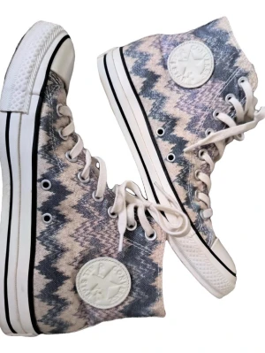 Converse All Star zigzag mönstrade - Säljer ett par Converse All Star high-tops med unikt zigzag-mönster i blått, beige och grått. Skorna har klassisk vit gummisula, rund tå och snörning. Ikonisk Converse-logga på sidan och platt sula. Perfekta för dig som vill sticka ut med dina sneakers.