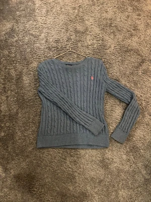 Blå kabelstickad tröja Polo Ralph Lauren - Kabelstickad blå tröja från Polo Ralph Lauren med rund halsringning. Passar dig som är ca 165-175. MVH