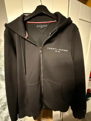 Tommy hillfiger kofta - Säljer en stilren svart Tommy Hilfiger zip-hoodie som bara är använd ett par gånger. Den är i väldigt fint skick, mjuk, varm och av hög kvalitet. Klassisk Hilfiger-design med broderad logga och en perfekt passform. En clean hoodie som funkar till allt och känns nästan som ny.