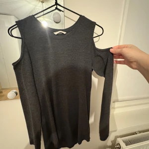 Mörkgrå långärmad topp med cold shoulder - Säljer  en mörkgrå långärmad topp med trendiga cold shoulder-detaljer. Toppen har rund halsringning och är tillverkad i ett mjukt, stretchigt material som sitter snyggt på kroppen. Perfekt för dig som vill ha en stilren men ändå unik look.