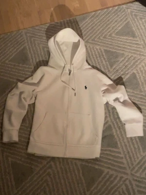 Ralph lauren zip - En vit ralph lauren zip hoodie som är riktigt stilig och snygg perfekt som en present nu när julen är nära. Riktigt skönt och tjockt material, väldigt väl omhändertagen. Taggen säger S men ralph lauren brukar vara stora i storleken så denna är storleksmässigt M! 🤞🙌