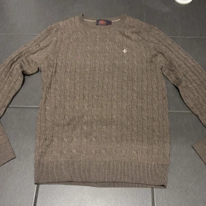 Beige kabelstickad tröja Morris M - Snygg beige kabelstickad tröja från Morris i 100% merinoull. Tröjan har rund hals, ribbade muddar och ett litet Morris-emblem broderat på bröstet. Perfekt för dig som gillar klassisk stil med en modern touch. Tröjan är helt oanvänd, jag säljer den pga av att den inte passade mig 