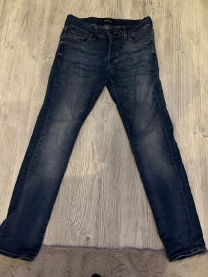 Mörkblå jeans från Jack & Jones - Snygga mörkblå jeans från Jack & Jones med klassisk femficksdesign och kontrastsömmar. Jeansen har en rak passform och normal midja, med subtila slitningar framtill och broderade bakfickor. Perfekt för dig som gillar stilrena och tidlösa jeans.