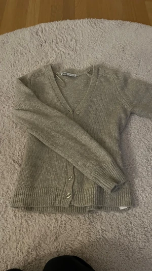 Beige stickad kofta från Zara - Snygg beige stickad kofta från Zara i storlek M. Koftan har v-ringning, långa ärmar och knappar framtill. Passar mig som ofta har s eller xs knappt använd skriv för mer bilder