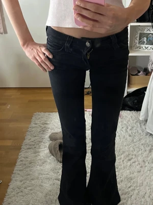 Svarta bootcut jeans från Cheap Monday - Säljer ett par svarta jeans från Cheap Monday med bootcut passform och låg midja. Har fickor, dragkedja och knapp framtill. Snyggt grafiskt märke baktill och rosa Cheap Monday-detalj vid linningen. Storlek 23/30!