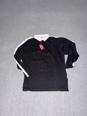 Långärmad Slazenger piké med vit krage - Helt ny långärmad piké från Slazenger i storlek S med vit krage och vita ränder längs ärmarna. Pikén har en klassisk look med kontrastfärgade detaljer och är tillverkad i mjuk bomull. Perfekt för dig som gillar sportig stil med en twist.