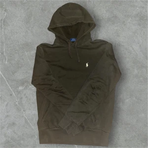 Brun hoodie från Polo Ralph Lauren - Snygg brun hoodie från Polo Ralph Lauren med klassisk logga broderad på bröstet. Tröjan har huva med snörning, känguruficka och långa ärmar. Tillverkad i mjuk bomull som är skön att ha på sig. Perfekt för dig som gillar stilrena och bekväma plagg.