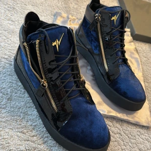 Helt nya Blå sneakers med dragkedja från Giuseppe zanotti  - Snygga blå sneakers från Giuseppe Zanotti med svarta detaljer och dragkedja på sidan. Skorna har en unik design med en kombination av glansigt och matt material. Perfekta för att ge din outfit en extra edge.
