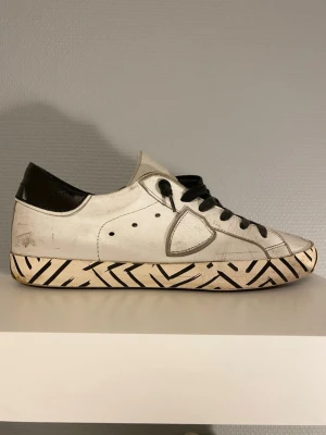 Philippe Model skor - Vita Philippe Model skor med svarta detaljer på sulan. Skorna kommer i stl 40 och är i bra skick, de mesta slitningarna är design. Undersulan är dock lagad med lim eftersom den brast lite vid hälen. Hör av er vid frågor!