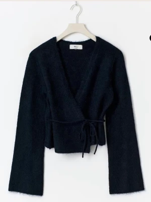 Mörkblå omlottkofta från GLAMOROUS - Snygg mörkblå omlottkofta från GLAMOROUS med croppad passform och långa ärmar. Koftan är stickad och har en mjuk, fluffig känsla. Knytband i midjan ger en cool detalj och v-ringad halsringning gör den extra stilren. Perfekt att styla med jeans eller kjol. Storlek M, helt oanvänd med prislapp kvar😊❤️