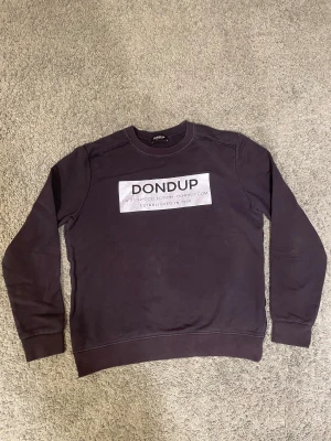 Dondup crewneck - Säljer denna riktigt feta dondup crewneck, den är äkta men är i använd skick och ser inga konstigheter med den alls. Ny pris 4000kr och säljer den för 1300kr. Höjden på tröjan är 64cm och midjan är 52 cm. Hör av dig om du vill ha mer bilder.