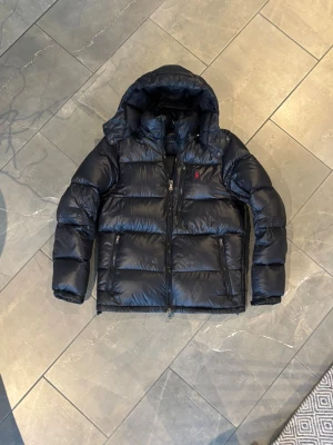 Jacka från Ralph lauren - olo Ralph Laurent jacka i size S, den är i svart/navy och glansig. Köptes för en stund sedan men är i fint skick ändå förutom ett litet hål som lagades på höger arm, det syns inte om man inte vet vart man ska kolla. Bara att höra av dig vid frågor eller funderingar.