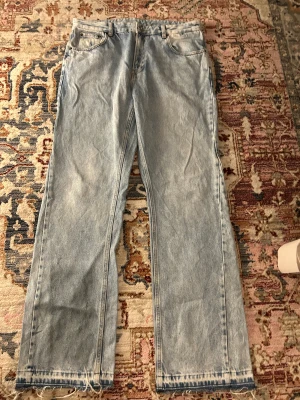Ljusa raka jeans från Zara, strl 46 - Säljer ett par ljusblå jeans från Zara i rak modell med normal passform. Jeansen har klassisk femficksdesign och råa, fransiga benslut för en avslappnad vibe. Materialet är 100% bomull och de har en enkel, tidlös look.