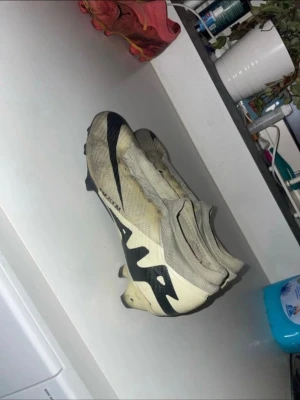 Nike Mercurial Air Zoom fotbollsskor - Säljer ett par Nike Mercurial Air Zoom fotbollsskor i vit och svart med coolt grafiskt tryck. Skorna har låg profil, platt sula med dobbar och är tillverkade i syntetmaterial för lätt känsla och bra grepp på planen. Perfekta för dig som vill ha snabba fötter och snygg stil på matchen.  Pris kan diskuteras… (Elite)