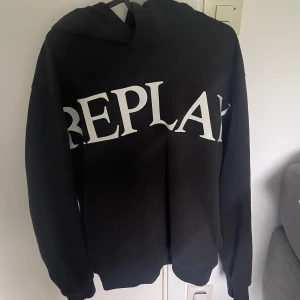 Svart hoodie från Replay  - Säljer en svart hoodie från Replay med stor vit logga över bröstet. Klassisk modell med huva och ribbade muddar. Perfekt för en avslappnad och stilren look. Knappt använd och säljer för att den aldrig får användning, pris går alltid att diskutera🤩