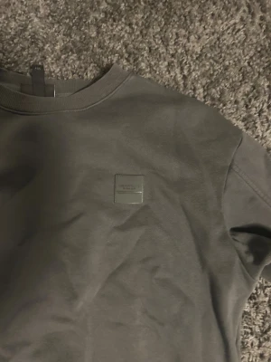 Mörkgrå sweatshirt Les Artists - Säljer en stilren mörkgrå sweatshirt från Les Artists. Tröjan har rund hals, ribbade muddar och en diskret patch med logga på bröstet. Tillverkad i mjuk bomull och har en relaxed fit som passar perfekt till jeans eller sweatpants.