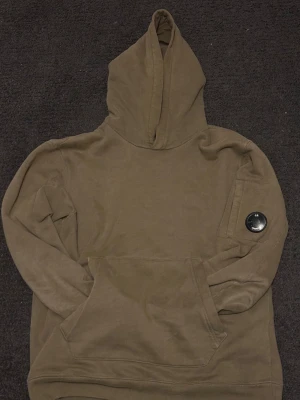 CP Company Hoodie olivgrön - Säljer denna riktigt snygga Cp Company hoodie i olivgrön färg. Väldigt bra skick har dock pyttelite vit färg på märket som man ser på bilden går säkert att få bort, nypris 1999kr. Skriv vid funderingar.
