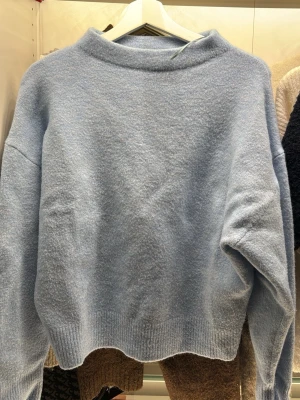 Ljusblå stickad tröja från Zara - Supermysig ljusblå stickad tröja från Zara med relaxed fit och ribbade muddar. Tröjan har en högre krage och långa ärmar, perfekt för lager på lager under kyliga dagar. Enkel och stilren design som är lätt att matcha.