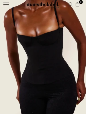 Svart korsett från Mars the label - Supersnygg svart korsett med smala axelband och markerad byst från Marshthelabel. Toppen har en tight passform som framhäver midjan och en stilren, minimalistisk look. Perfekt att styla med jeans eller kjol för en trendig vibe. Stolek UK 4.