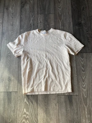 Beige t-shirt från Zara i bomull - Snygg beige t-shirt från Zara i mjuk bomull. Klassisk rund hals och korta ärmar, perfekt för en clean och enkel stil. Passformen är normal och färgen är neutral, vilket gör den lätt att matcha med allt. En basic tee som alltid funkar.