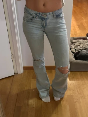 Nelly jeans - Snygga ljusblå bootcut jeans med slitna hål på båda knäna och coola detaljer på bakfickorna från Nelly. Storlek 34, är 164 lång. Nypris 700kr. Mycket fint skick men lite slitna längst ner. 
