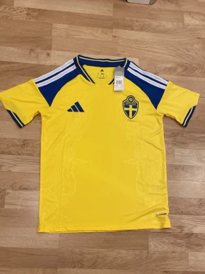 Sverige hemmatröja 25/26 - Sveriges nya hemmatröja i Storlek S. Tröjan är helt ny och har adidas samt landslagsmärke på bröstet. Vita ränder på axlarna och snygga nyanser på tröjan. Perfekt till VM-kvalet. 