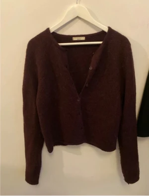Vinröd kofta från gina - Säljer en mysig vinröd kofta från gina med lång ärm och knappar framtill. Koftan har en enkel, klassisk design och är tillverkad i mjukt material som passar perfekt för kyliga dagar. Perfekt att slänga över en t-shirt eller linne.
