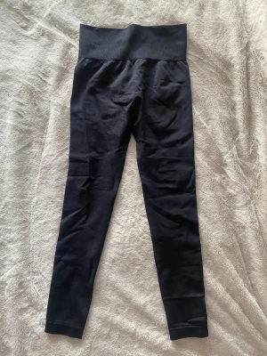 Svarta scrunch leggings med hög midja - Säljer ett par svarta leggings med scrunch-detalj bak och bred, ribbad hög midja. De är tighta och gjorda i stretchigt syntetmaterial som sitter snyggt och bekvämt. Perfekta för gymmet eller chill hemma. 