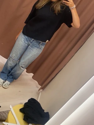 Svart stickad tröja med kort ärm - Svart stickad tröja med korta ärmar och rund hals. Enkel och clean design som funkar till jeans eller kjol. Mjuk och skön känsla, perfekt för dig som gillar minimalistisk stil. Tröjan har en normal passform och är lätt att matcha med olika outfits.