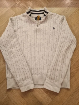 Vit stickad tröja Polo Ralph Lauren - Snygg vit stickad tröja från Polo Ralph Lauren i storlek Xl i barn (S). Tröjan har kabelstickat mönster, ribbade muddar och krage med svarta ränder. Half zip-dragkedja framtill och klassisk broderad logga på bröstet.  Nypris 1799