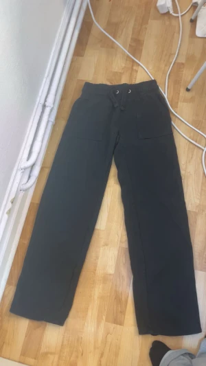 Svarta mjukisbyxor med snörning - Svarta mjukisbyxor med elastisk midja och snörning framtill. Byxorna har raka ben och stora fickor både fram och bak. Perfekta för en chill och avslappnad stil. Tillverkade i mjukt bomullsmaterial för extra komfort.