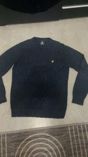 Mörkblå stickad tröja Lyle & Scott M - Snygg mörkblå tröja från Lyle & Scott i storlek M. Tröjan har ett klassiskt rund hals och långärmade ärmar. På bröstet finns den ikoniska gula fågeln. Perfekt inför vintern då den är väldigt varm och skön. Pris kan sänkas mycket så hör av dig. Den är helt ny och oanvänd. 