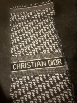 Christian Dior svartvit mönstrad väst - Exklusiv halsduk från Christian Dior med svartvitt mönster och tydlig logga framtill. Västen är stickad i en lyxig blandning av 65% silke och 35% kashmir, vilket gör den både mjuk och elegant. Snyggt grafiskt mönster och klassisk form.