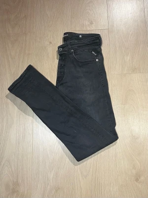Svarta Replay Anbass jeans slim fit - Snygga svarta Replay Anbass jeans med slim fit och klassisk femficksdesign. Jeansen har en modern, smal siluett och är tillverkade i stretchigt denim för extra komfort. Perfekta för dig som gillar stilrena och tidlösa jeans med en cool vibe.