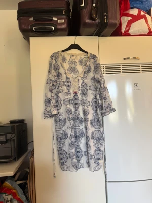 Odd Molly vit och blå paisleyklänning - Supersöt kortklänning från Odd Molly i vitt med blått paisleymönster. Klänningen har v-ringning med spetskant, snörning framtill och en liten rosett. Långa ärmar med lätt volang och knytband i midjan. Luftigt material, perfekt för varma dagar. Storlek 4 som enligt deras storleksguide motsvarar en L/XL. Mycket fint skick, jag hittar inga synliga anmärkningar eller defekter. 