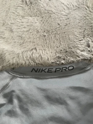 Nike Pro Dri-Fit grå träningströja - Nike Pro Dri-Fit t-shirt i ljusgrått med svart Nike-logga på bröstet. Tröjan har tight passform och är tillverkad i ett stretchigt, syntetiskt material som andas. Perfekt för intensiva träningspass och sportaktiviteter.