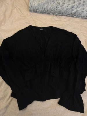 Svart volangblus med v-ringning - Säljer en svart blus från Gina Tricot med v-ringning och volangdetaljer framtill. Använd en gång, storlek M